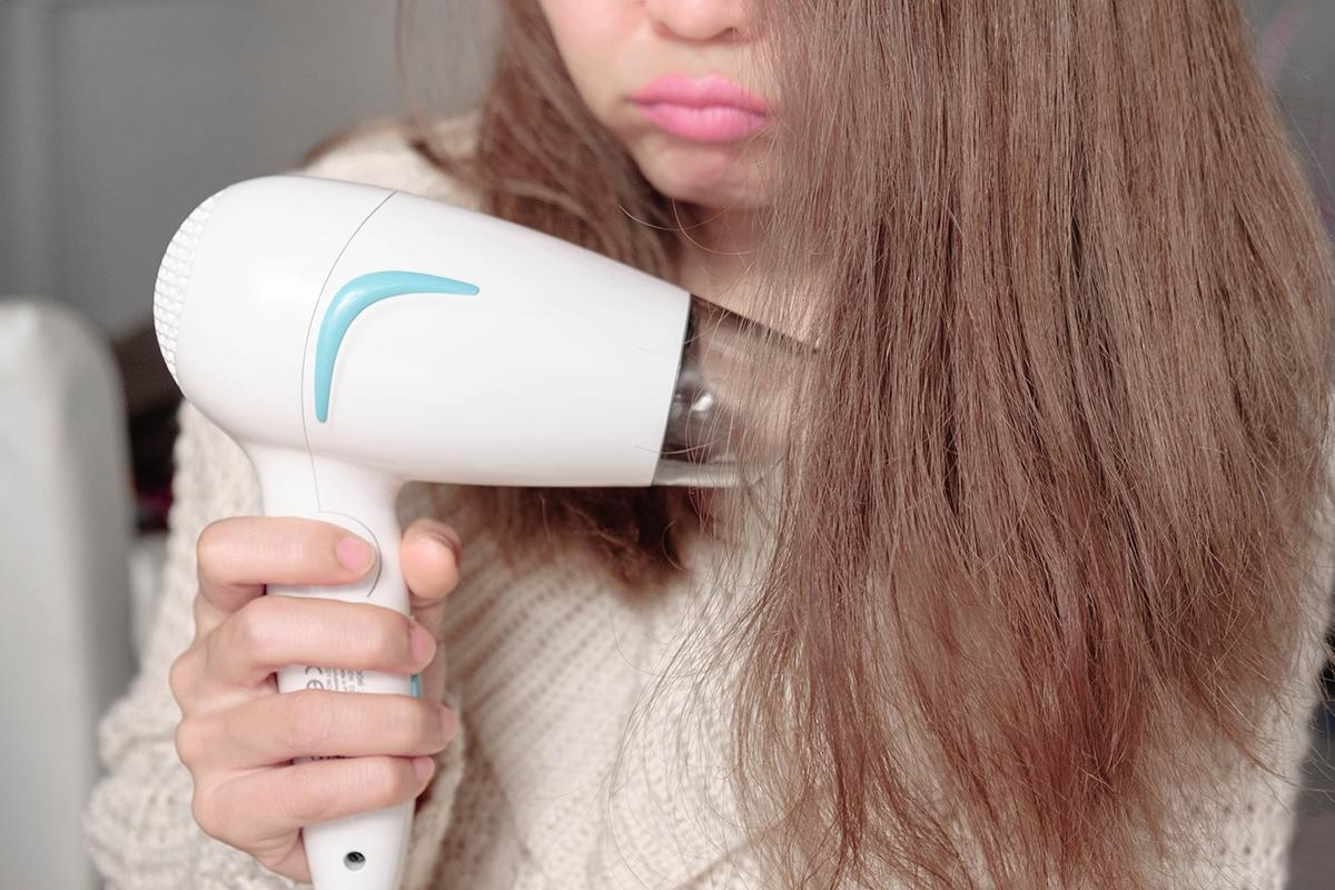 Asian woman blow drying frizzy, colored hair