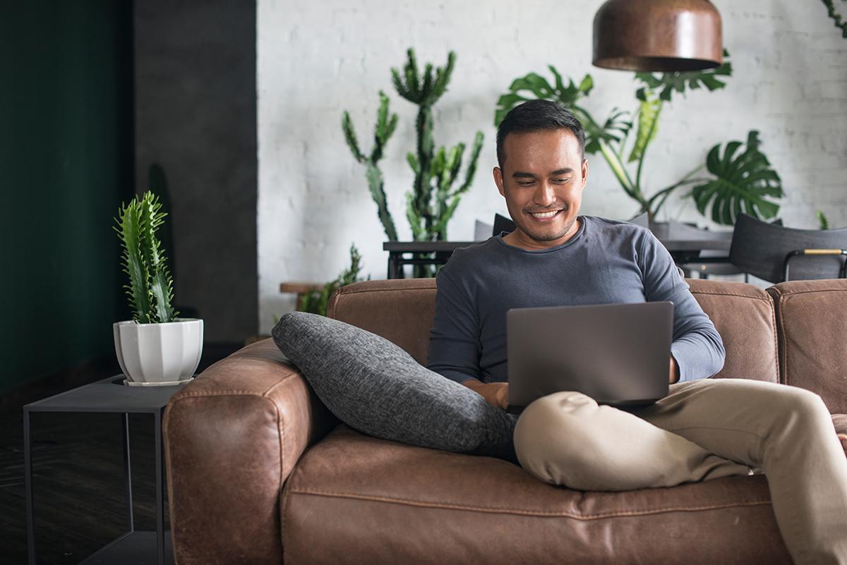 A man smiling in front of laptop on brown couch