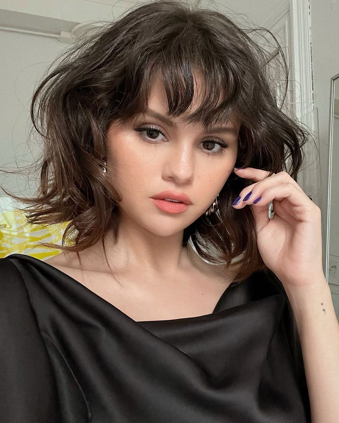 Selena Gomez in a black blouse with short bob and wispy bangs.