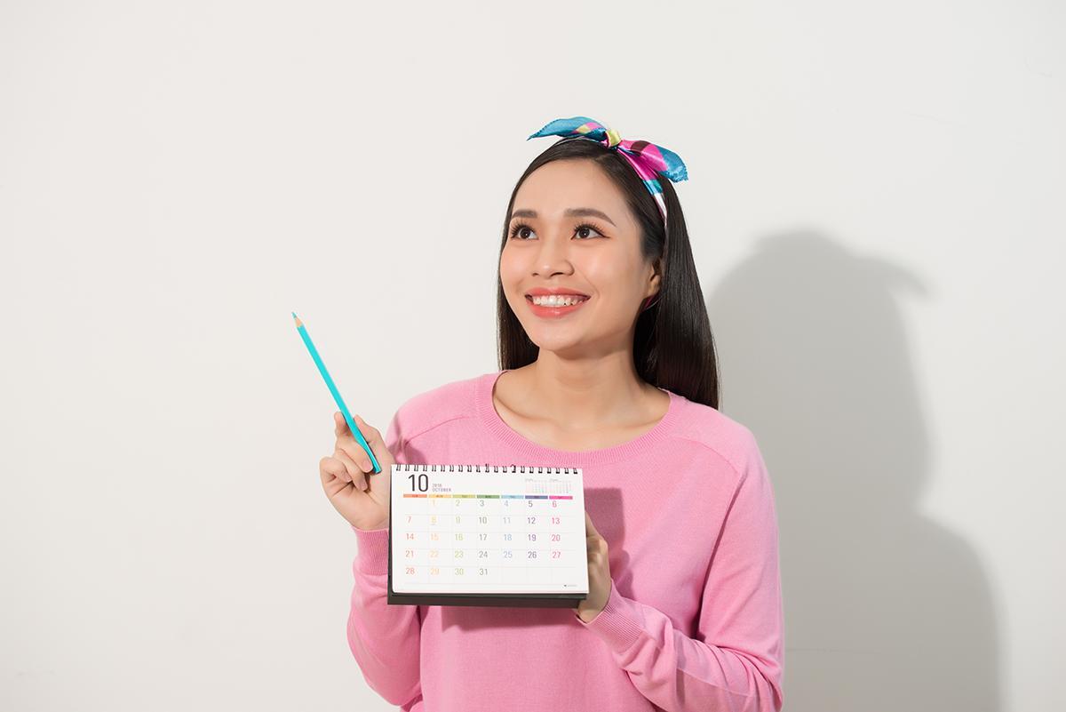 Asian girl in pink sweatshirt holding desk calendar