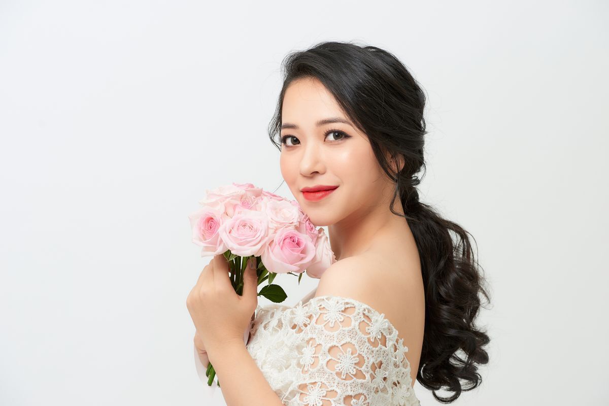 Asian bride holding bouquet against white background