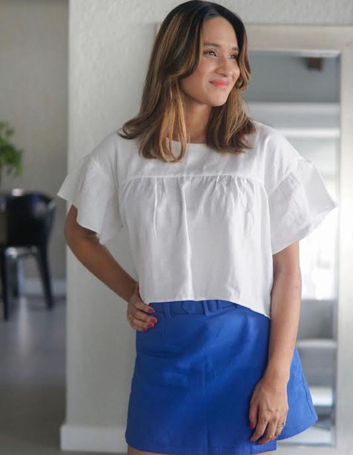 Asian woman in a white shirt and blue skirt with one hand on her waist and smiling while looking away.