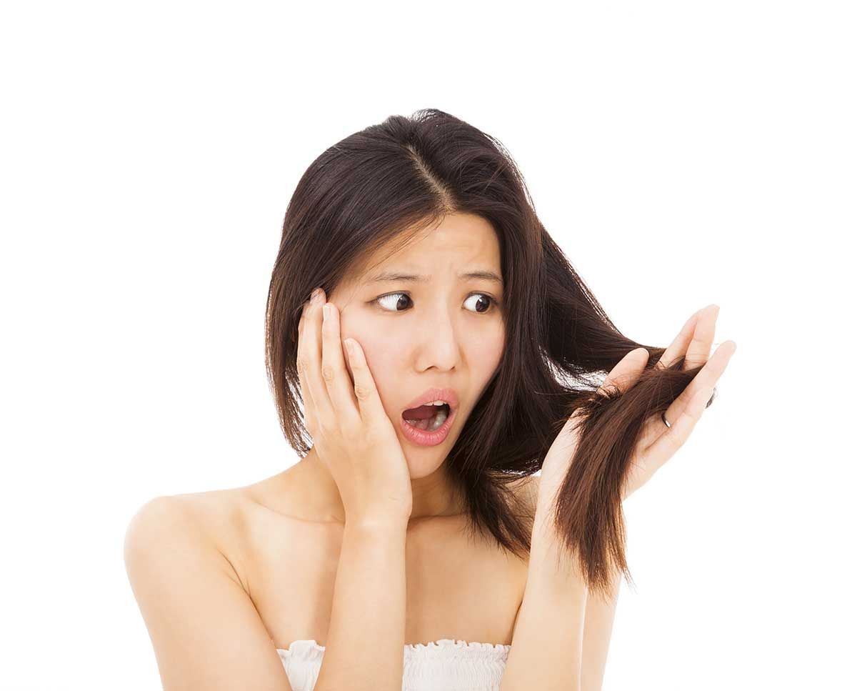 Asian woman looking at her dry hair