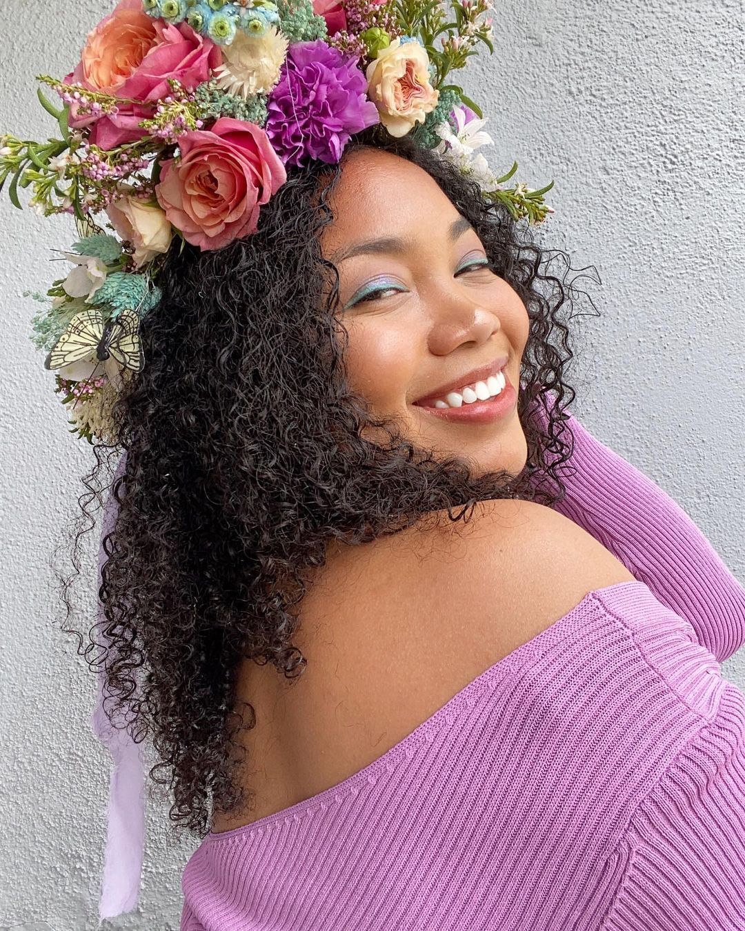 Woman with purple sweater and flower crown smiling to the camera.