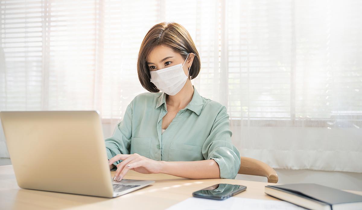 Asian woman with mask working on laptop