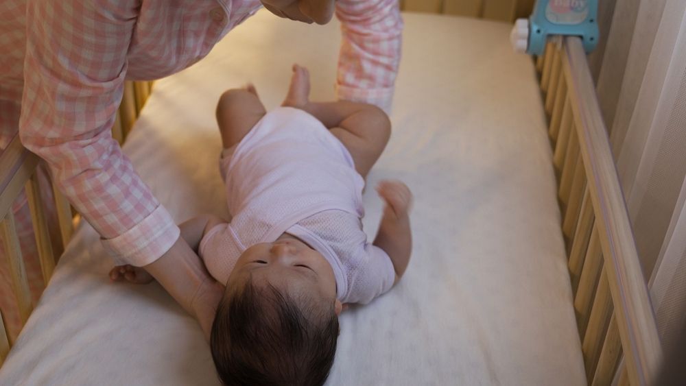 Woman in pajamas laying baby in crib for bedtime.