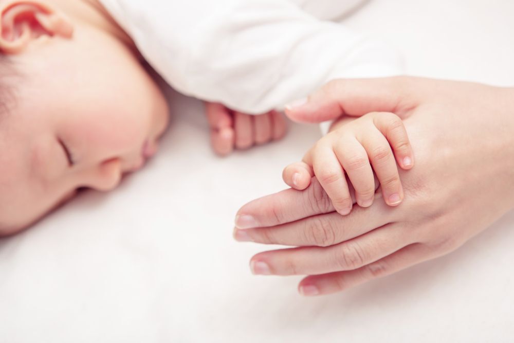 Sleeping baby holding its mother’s hand.