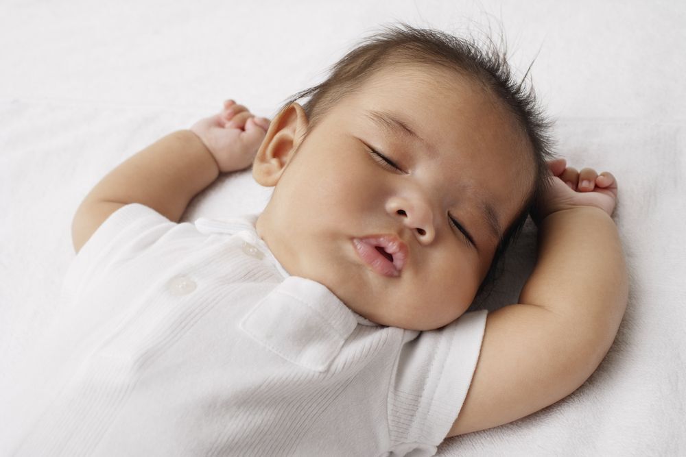 Sleeping baby on its back, with arms raised.