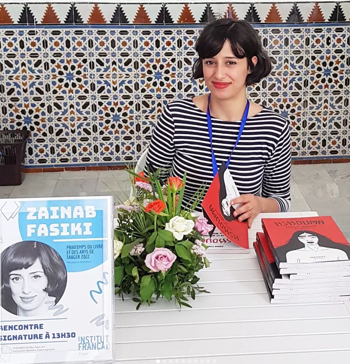 Zainab Fasiki poses with books while sitting down. 