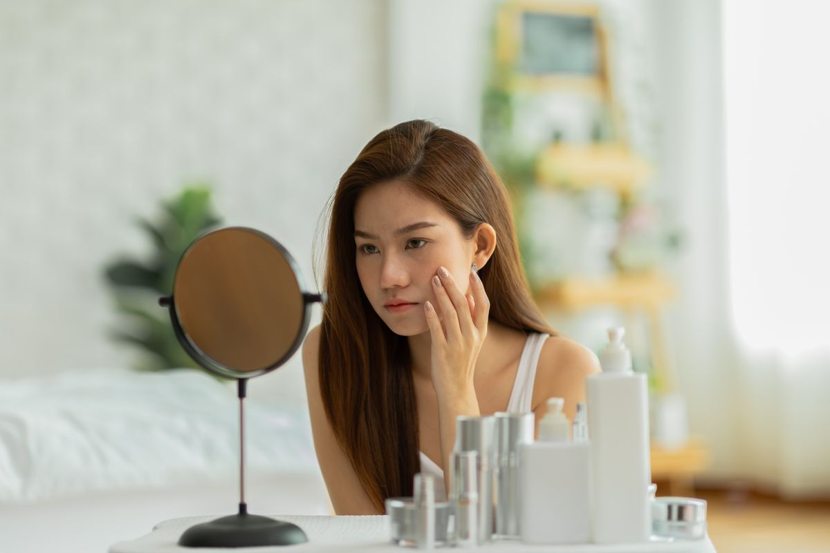 Asian woman worried about skin in the mirror.