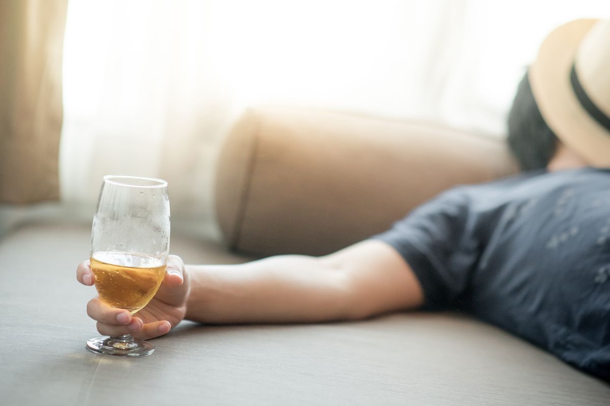 A man with a hat over his face holds a glass of beer