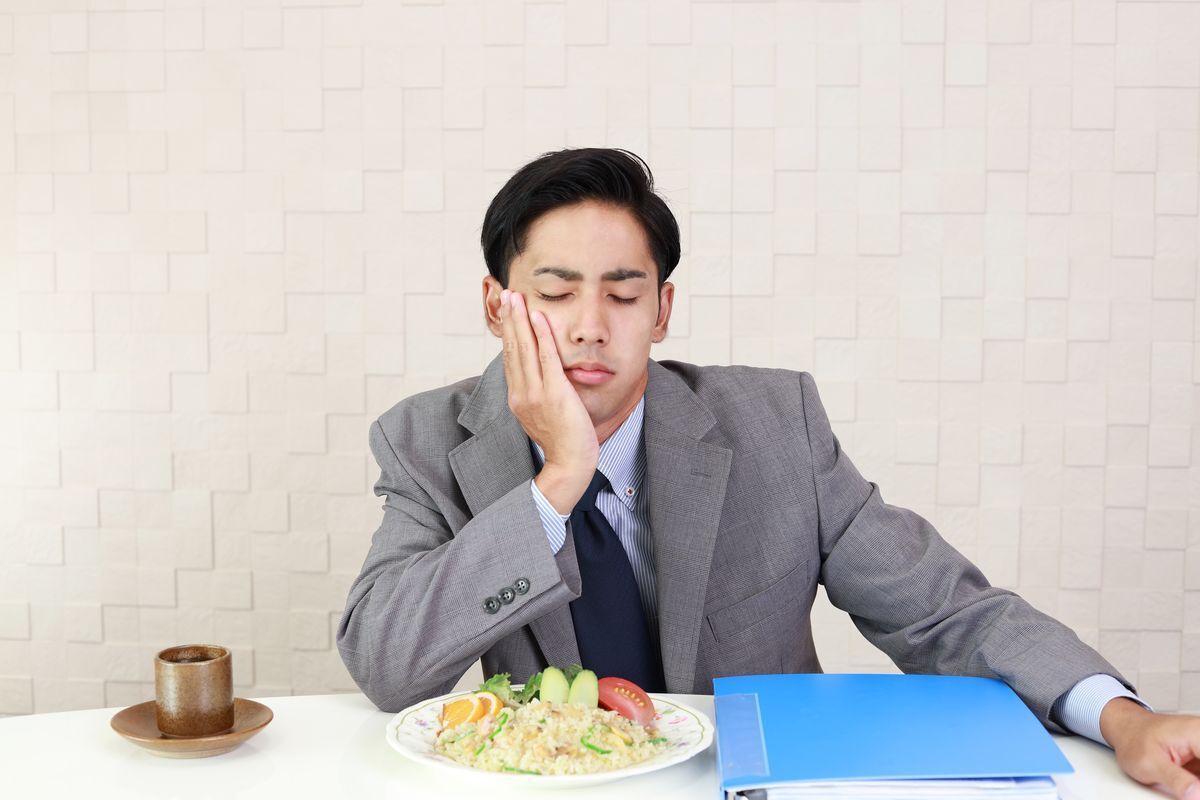 A man with his hand on his face sits in front of a meal