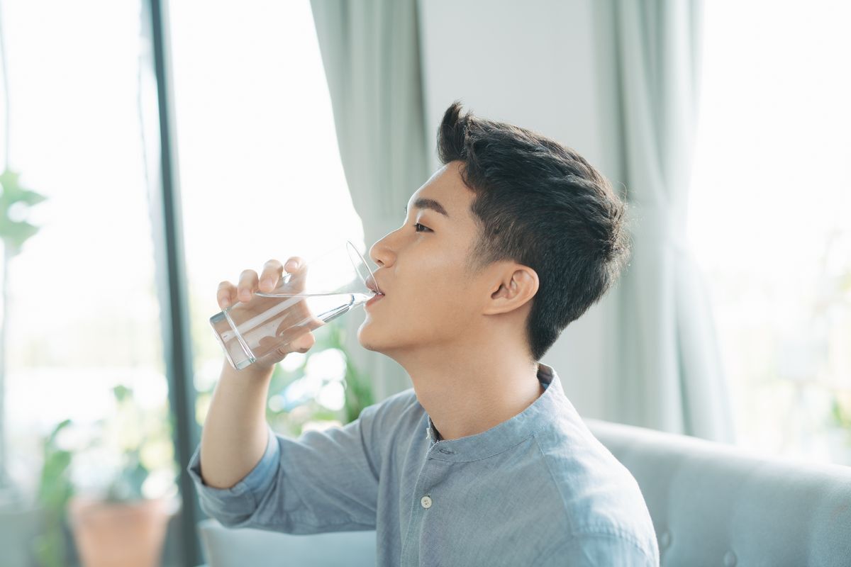 A man with his arm outstretched holds a glass of water