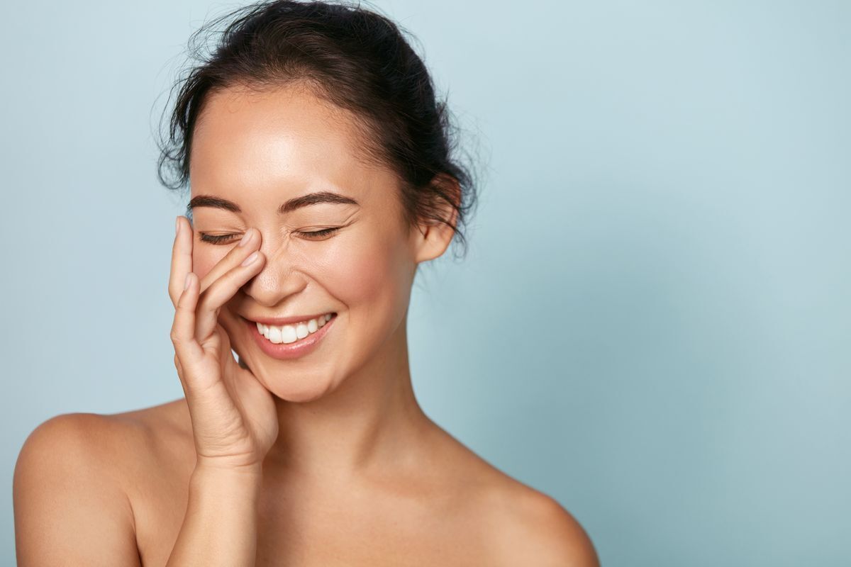 Filipino woman touching her hydrated face, smiling.
