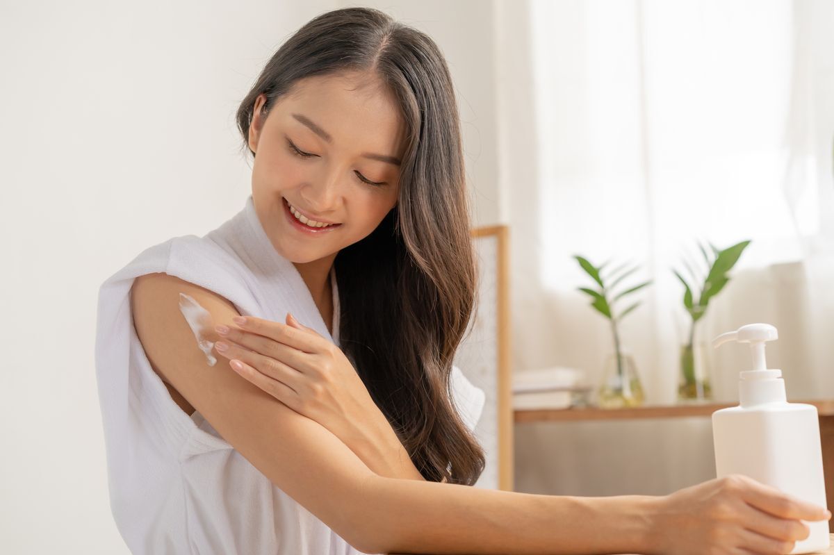 An Asian woman applying lotion on her arms.