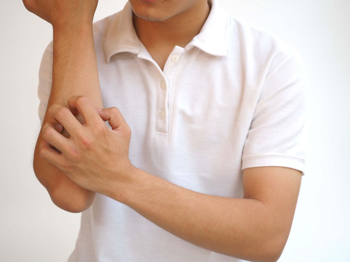 Man in a white shirt; scratching his arm.