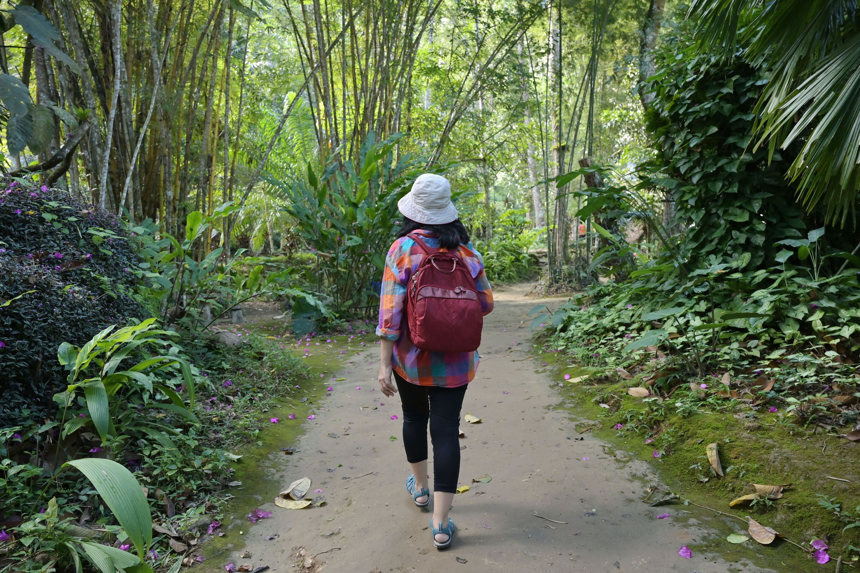 Asian woman wearing leggings and a bucket hat is walking in the park.