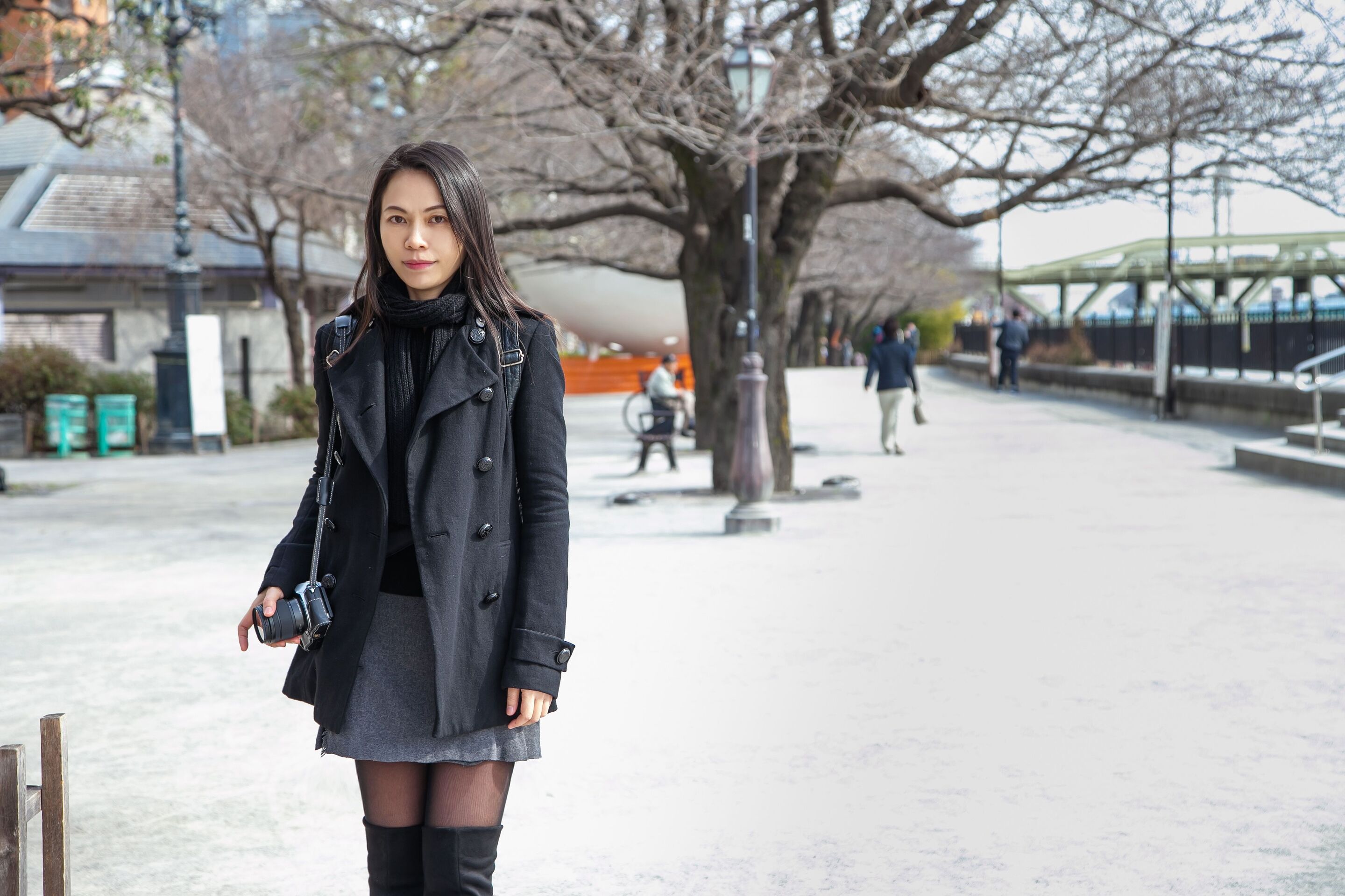 Asian woman wearing black jacket, gray skirt, and tights. 