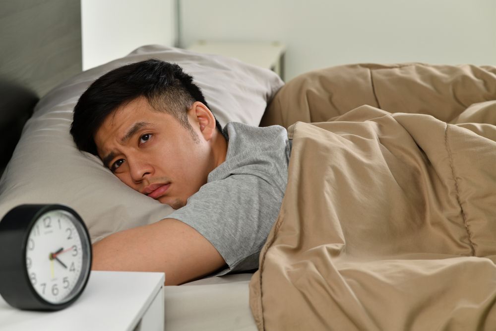 A young Asian man lying in bed awake. 