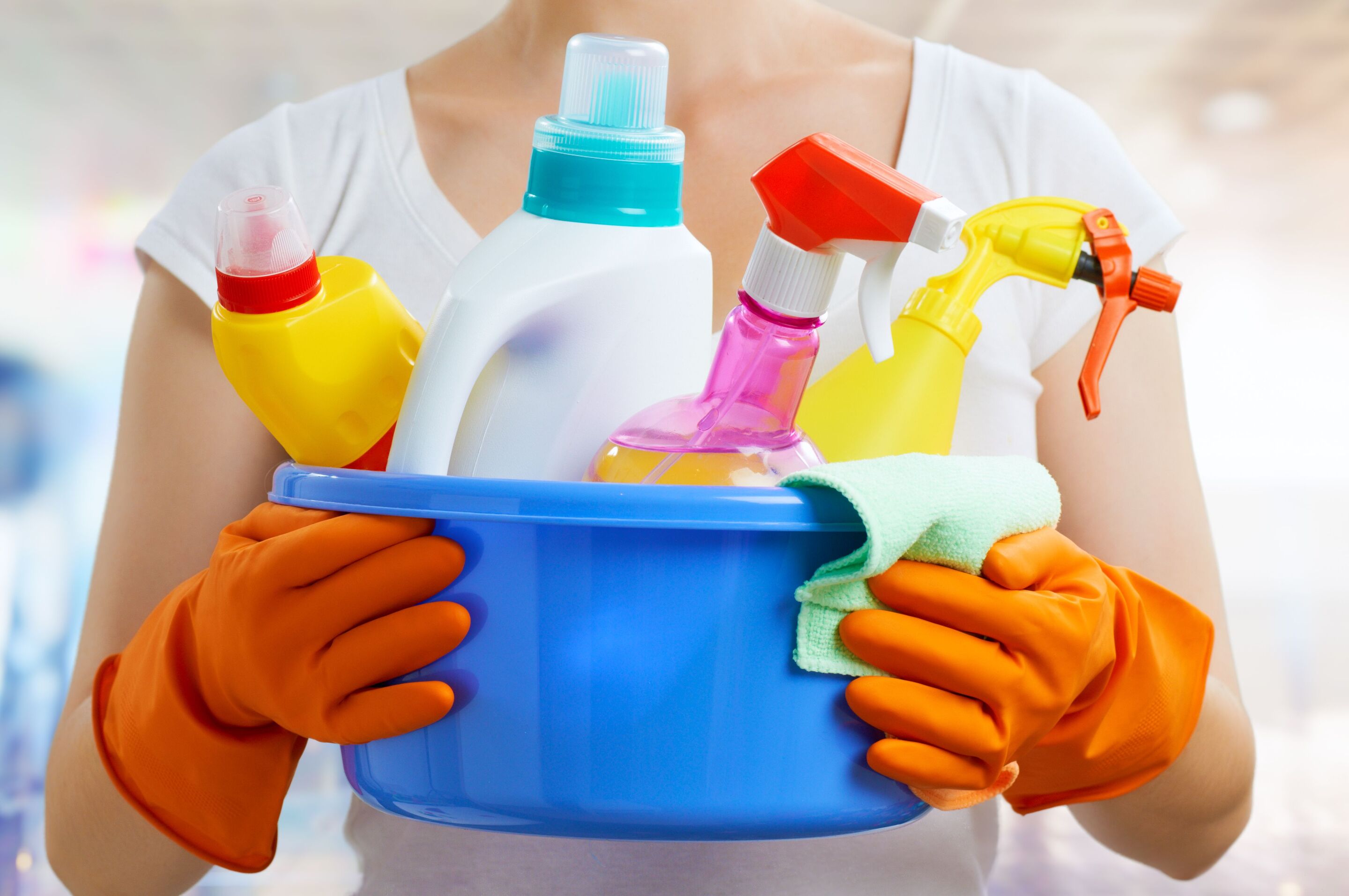Woman wearing gloves, holding a tub of different detergent bottles