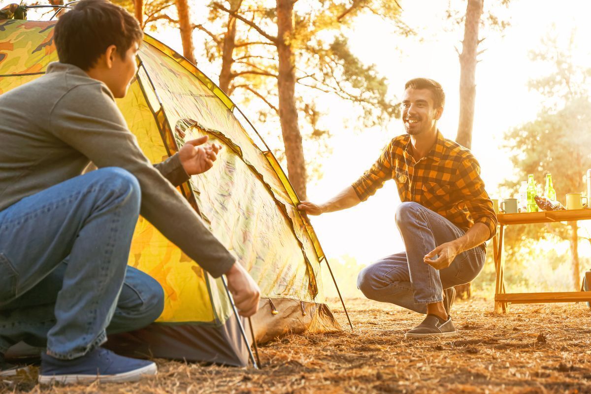 Two men happily pitching a tent outdoors against bright sunlight.