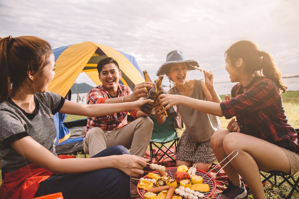 Friends happily drinking beer and grilling food while camping outdoors.