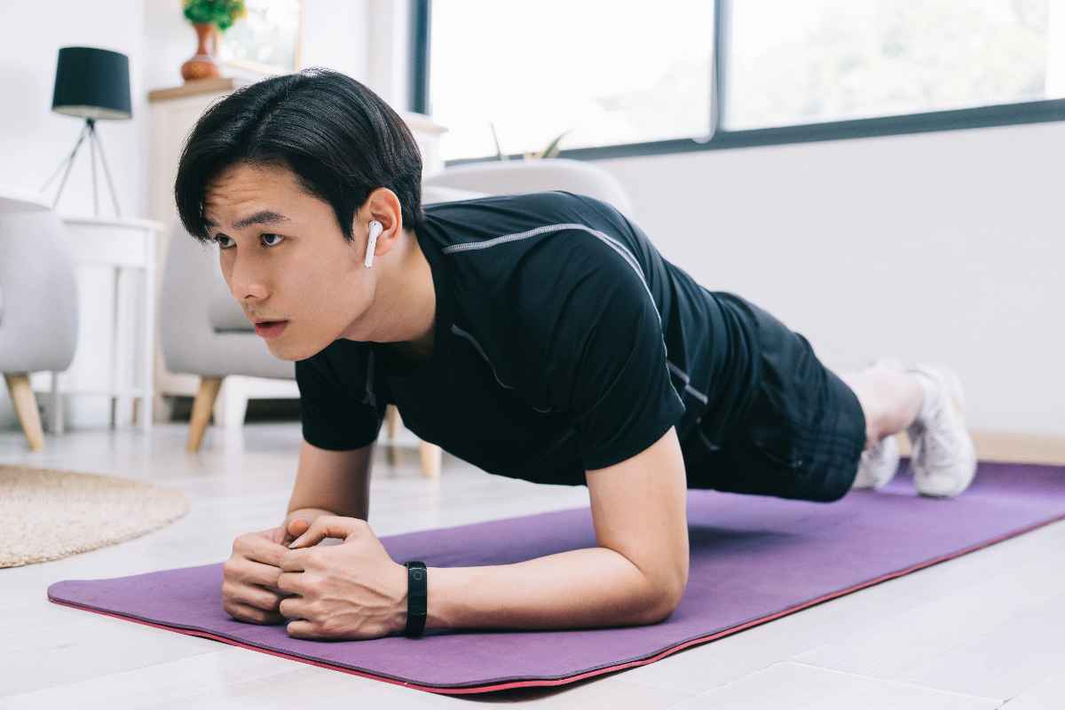 A young man planking on his forearms on a purple mat. 
