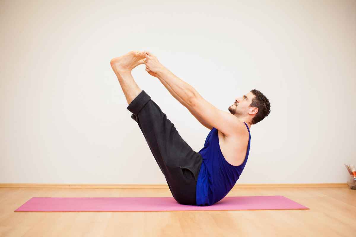 A man performing a boat pose on a pink yoga mat. 
