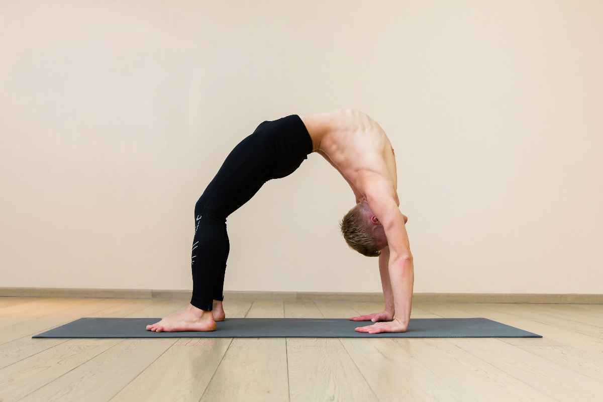 A man practicing a backbend on a grey exercise mat.