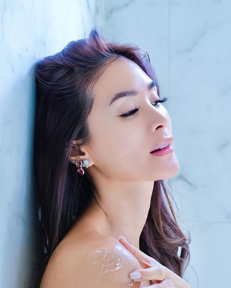 Asian woman with burgundy hair leaning on a wall