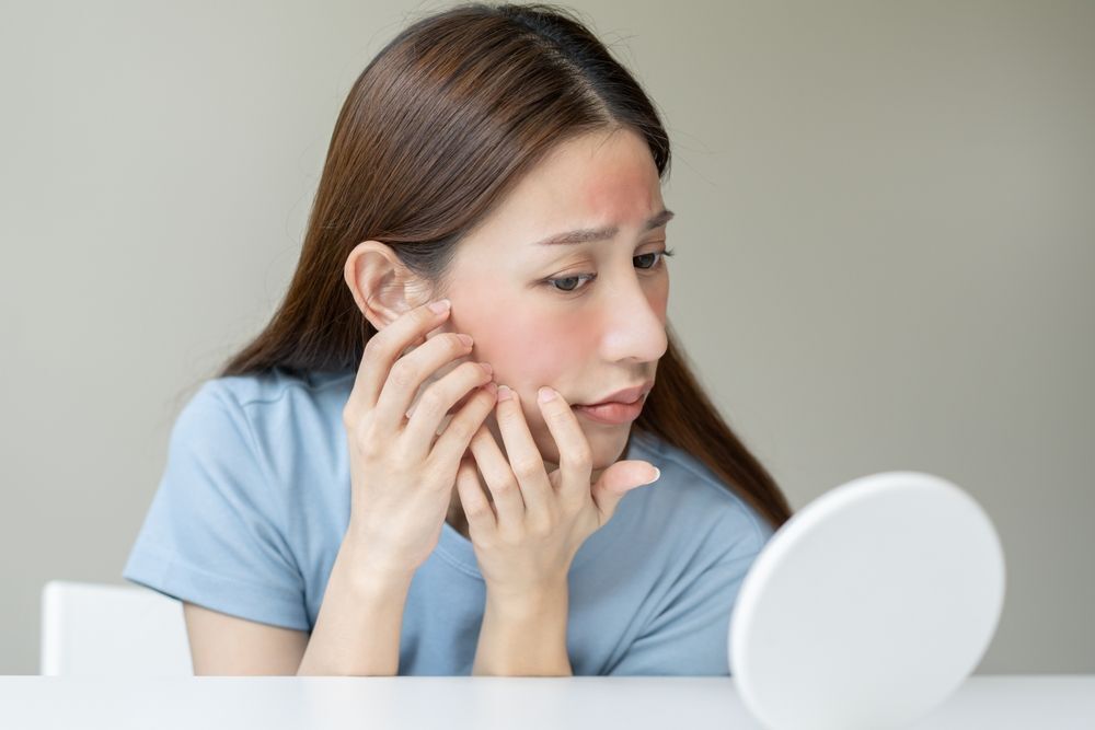 Asian woman with facial redness looking at a mirror, worried.