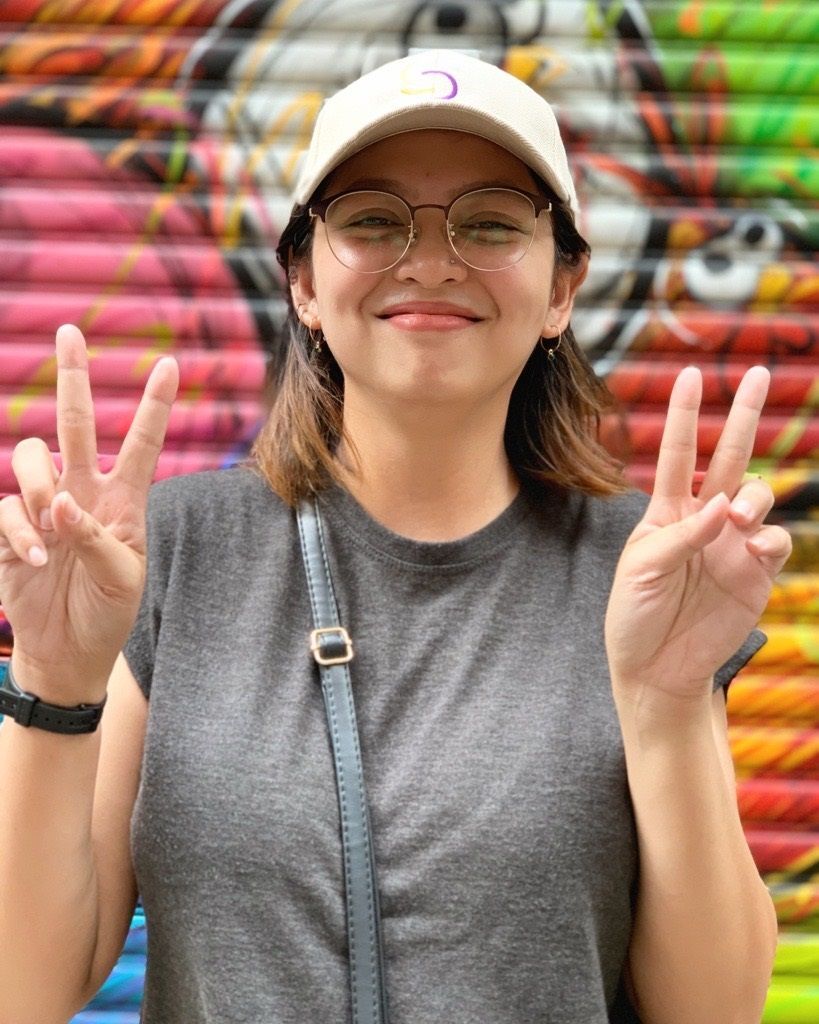 Smiling woman wearing glasses, white baseball cap, and gray T-shirt.