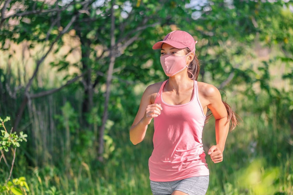 Asian woman running outside in the sun whilst wearing a pink cap, mask, and top.