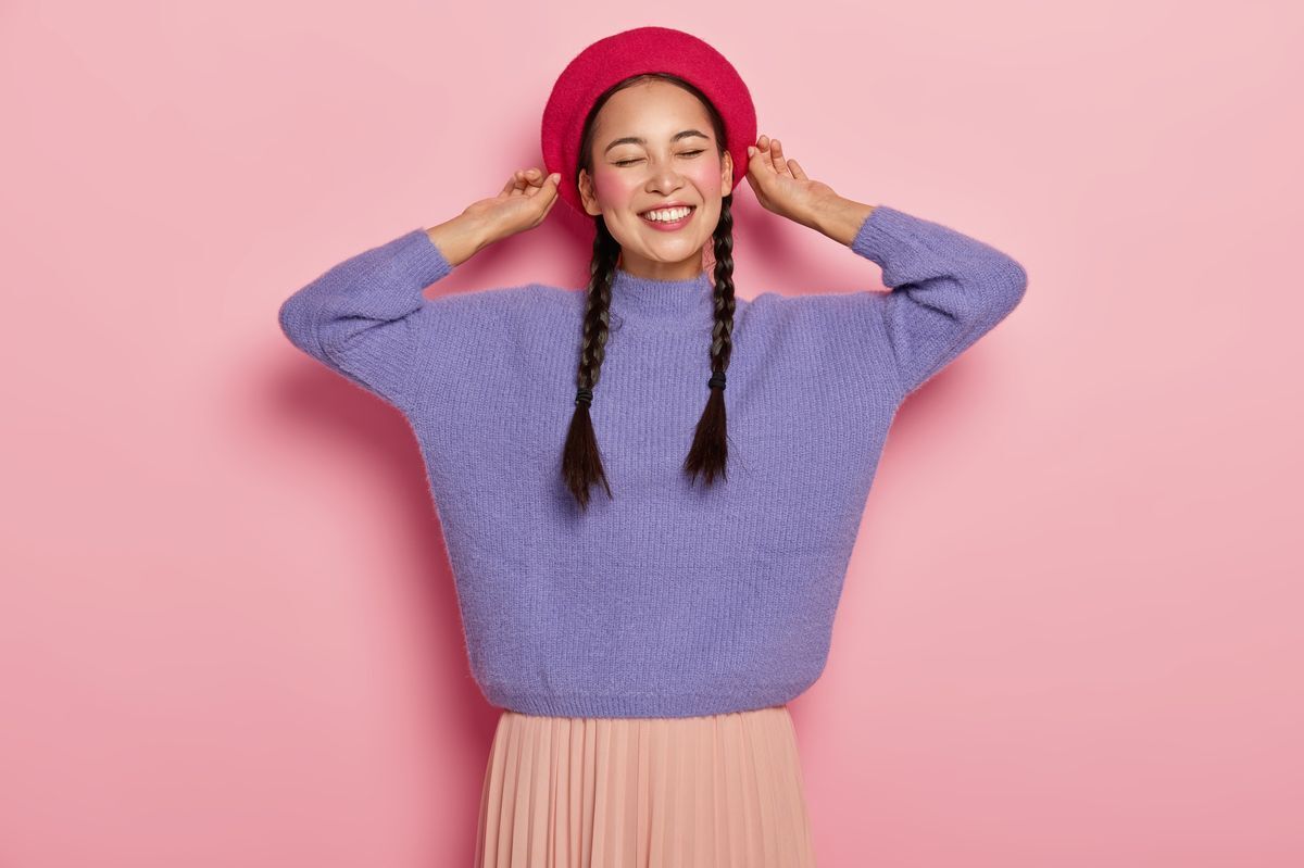 Asian woman holding onto a red beret while brightly smiling