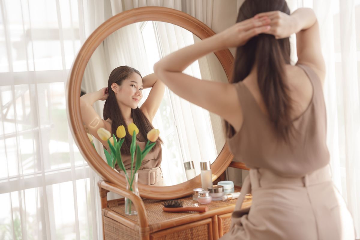 Woman tying her hair in front of a mirror. 