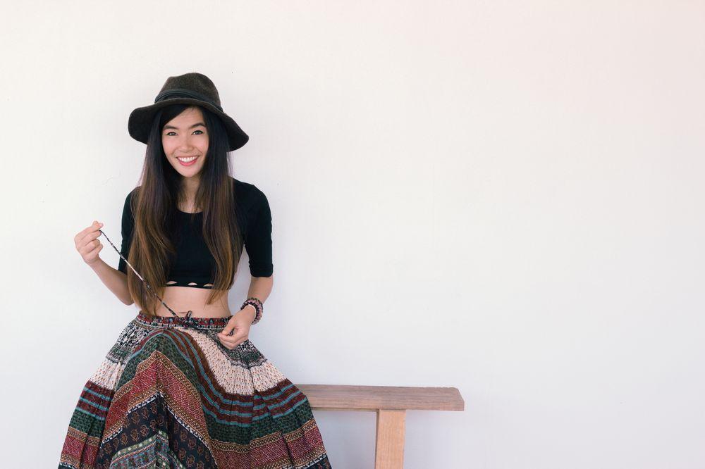 Asian woman in a black top and printed skirt sitting on a bench