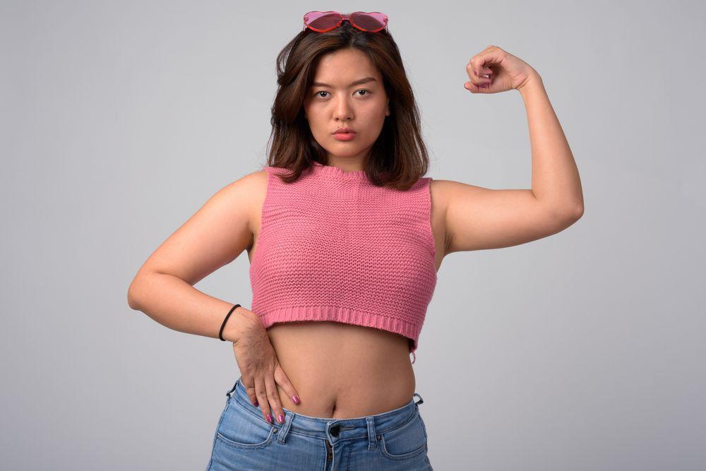 Confident Asian woman in pink knit cropped top and jeans