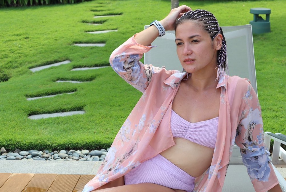 Asian woman wearing a loose shirt over a two piece bikini with high waisted bottom.