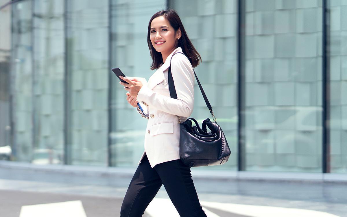 Asian career woman crossing the street with bag and phone