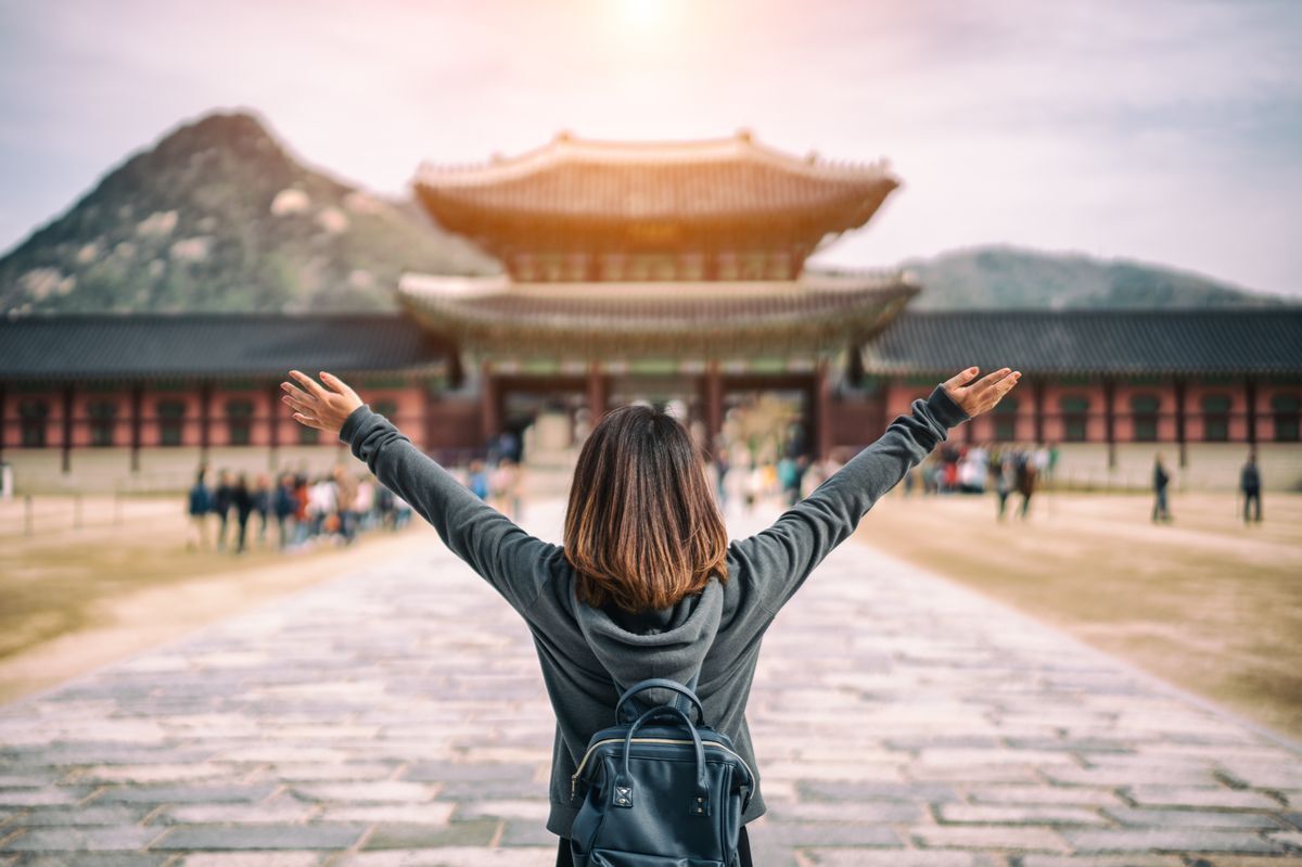 Asian woman traveler with arms outstretched facing a palace in South Korea