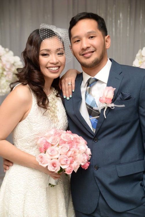 Smiling Asian bride holding a bouquet of pink flowers and smiling Asian groom in a navy blue suit and pink boutonnière.