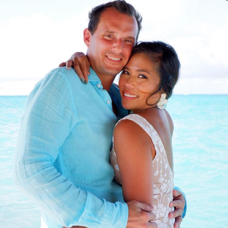 Smiling Asian bride and Caucasian groom against an ocean view.