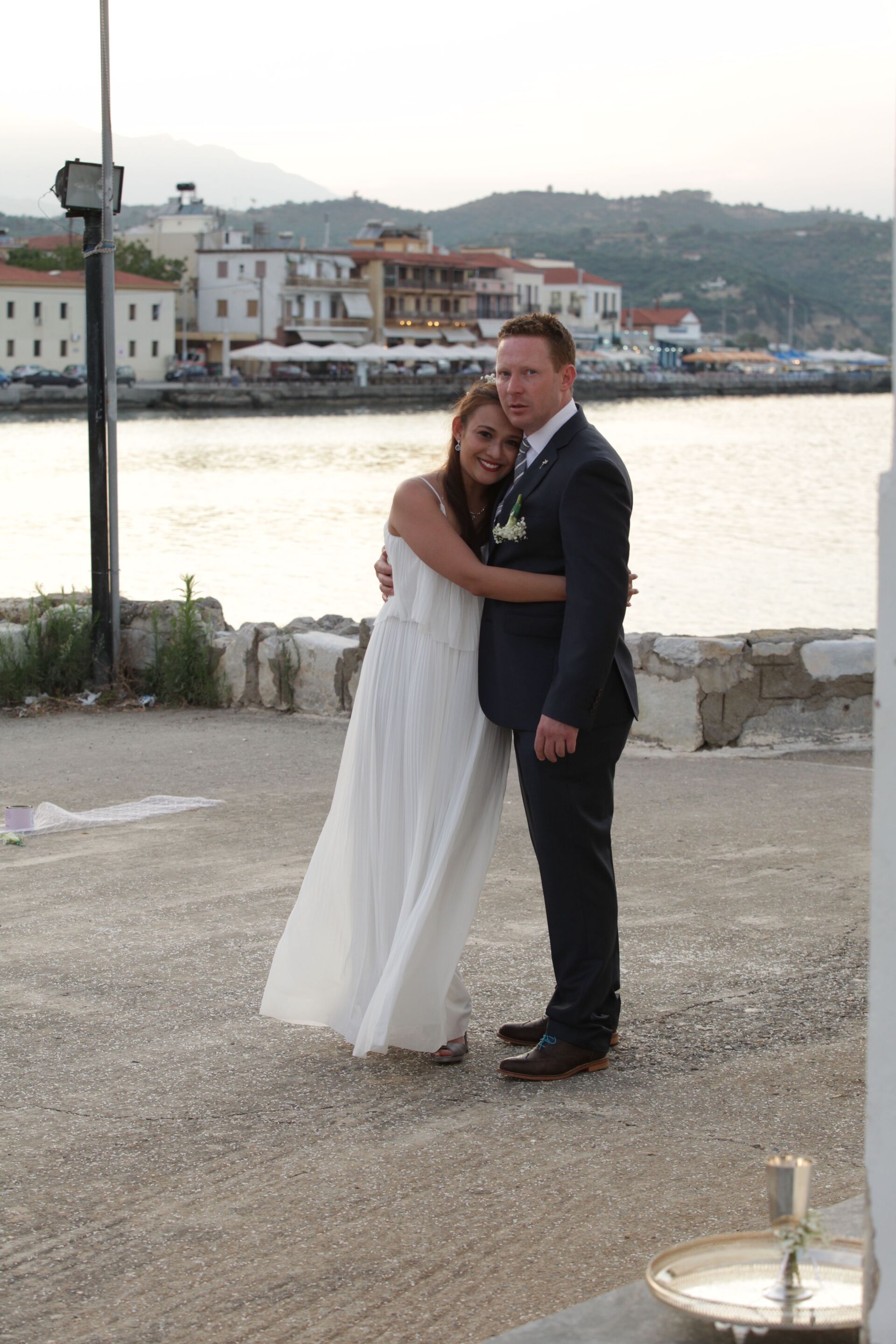 Smiling Asian bride and Caucasian groom against a harbor view.