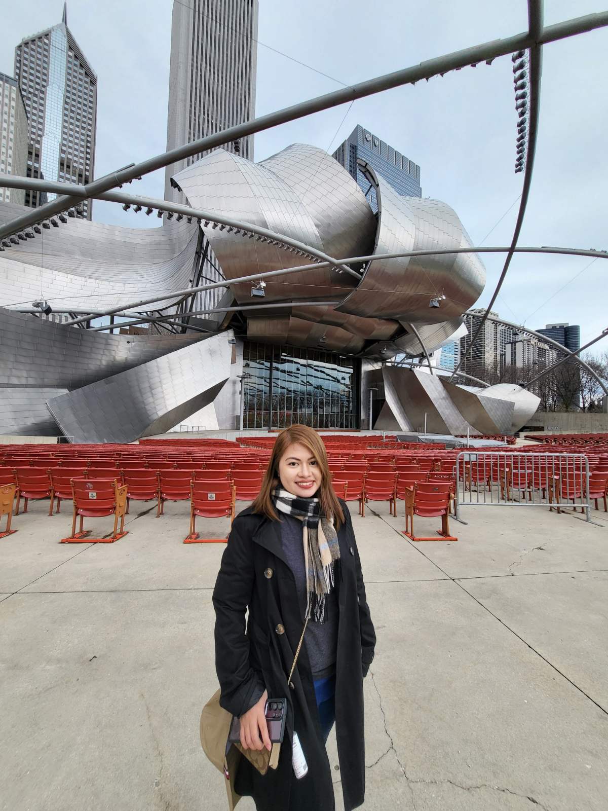 Asian woman in a black coat posing in front of a steel building.