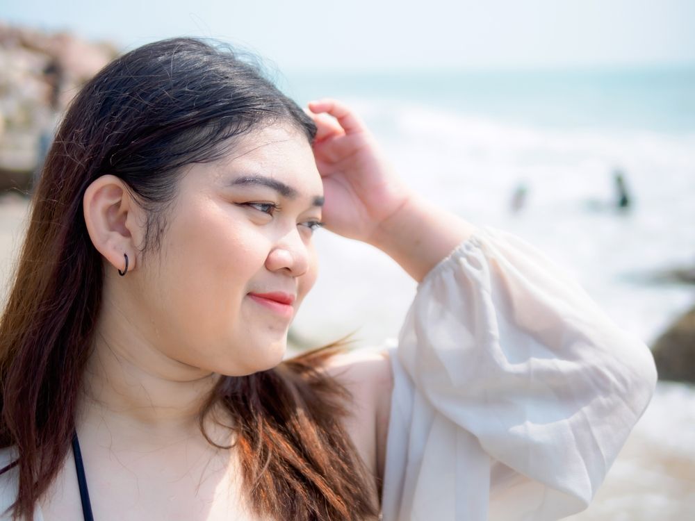 Woman in a black bikini smiling and posing at the beach.