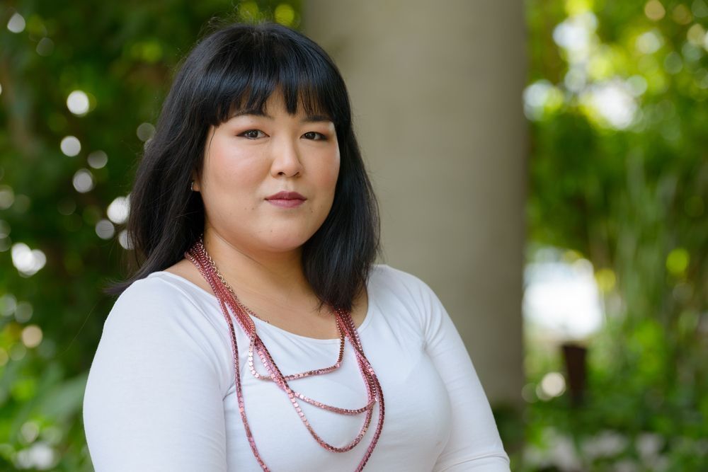 Woman in white bodycon dress and red necklace smiling at the camera.