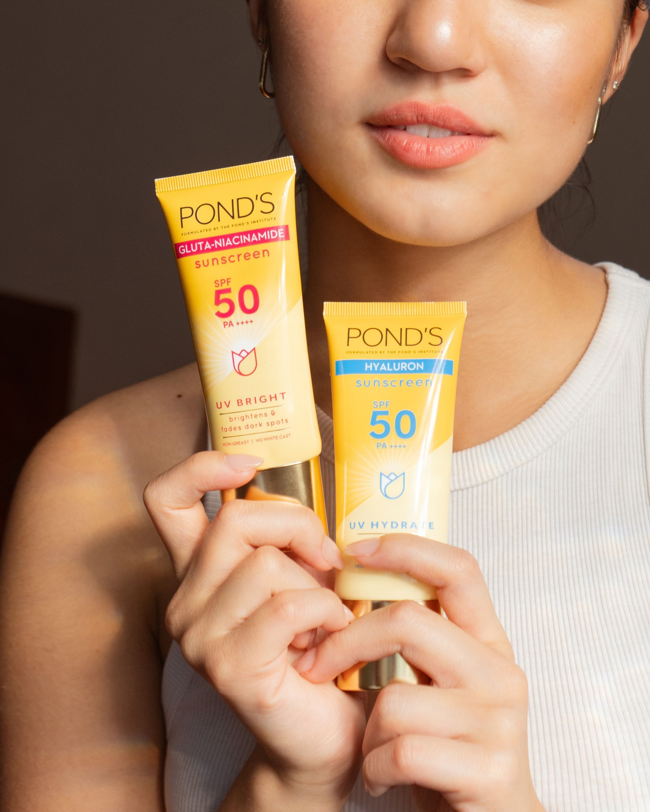 Closeup of an Asian woman holding two sunscreen products.