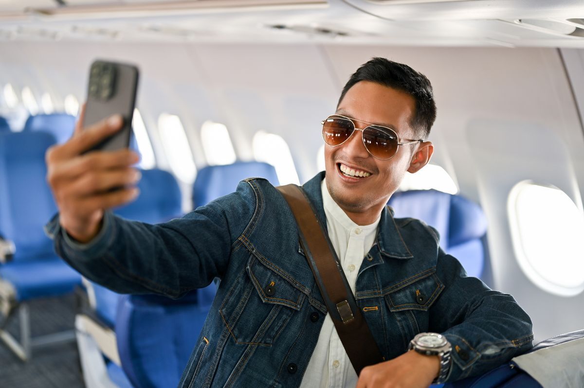 Man on a plane smiling and taking a photo of himself.