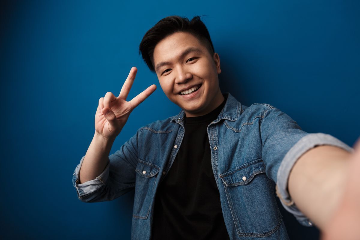 Asian man happily taking a photo of himself against a blue background. 