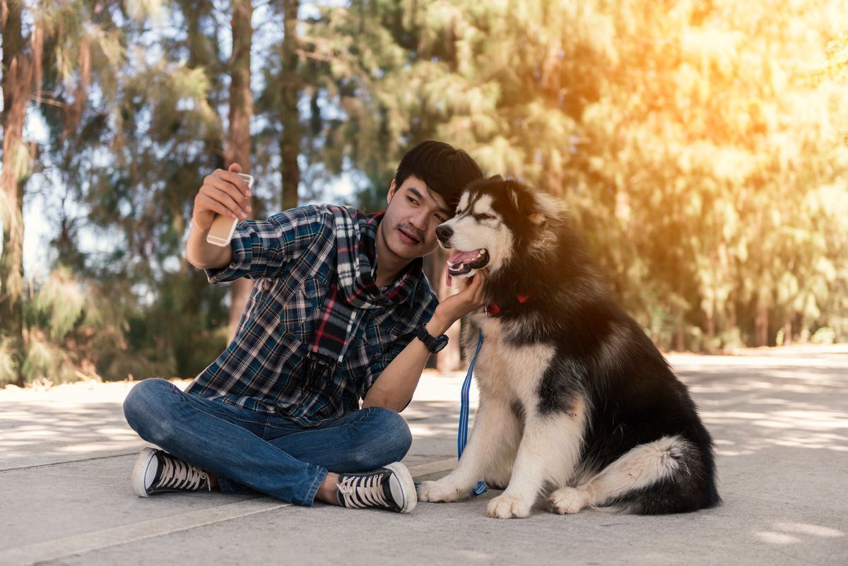 Young man happily taking a photo of himself and his dog outdoors. 